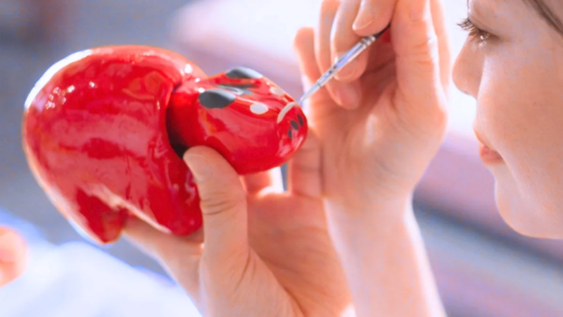 女性が赤い置物に細い筆で丁寧に絵付けをしている画像