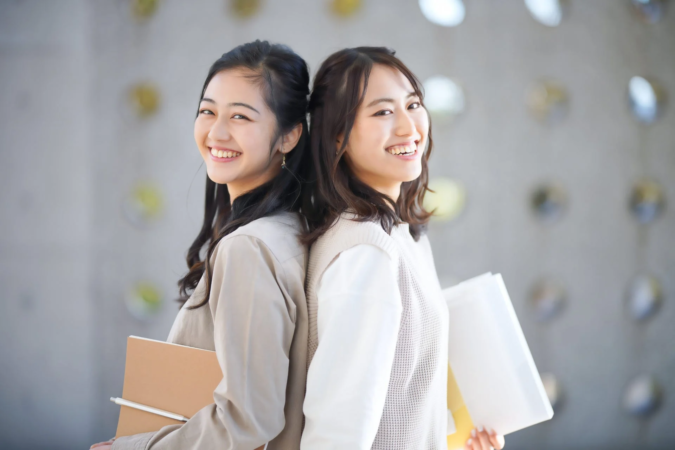 笑顔で背中合わせに立つ2人の若い女性