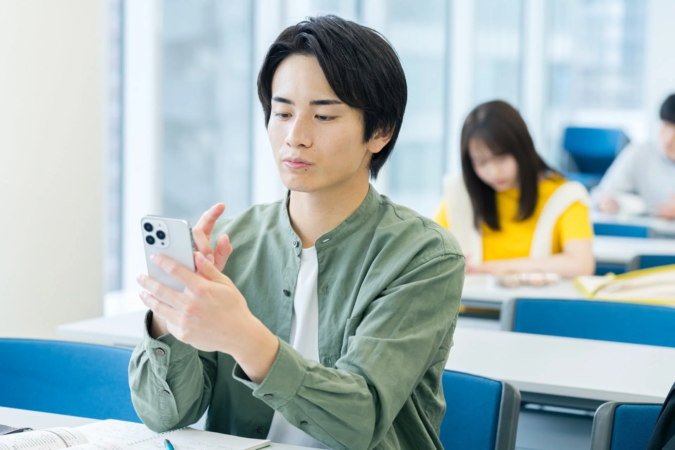 教室で若い男性がスマホを操作している様子