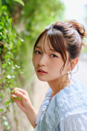 緑豊かな背景の中でカメラを見つめる水色の服を着た若い女性