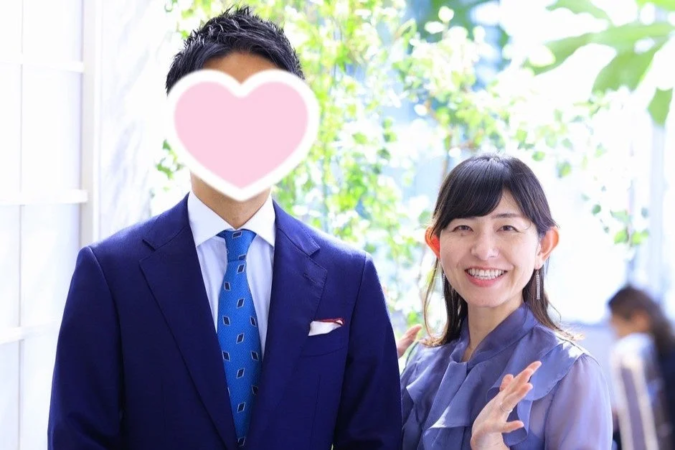 青いスーツ姿の男性と、笑顔でカメラを見つめる紫色のブラウスを着た女性のツーショットです。