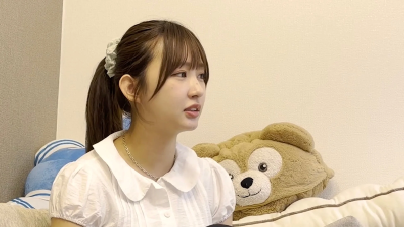 白いブラウスを着てポニーテールにした若い女性が、横を向いて座っています