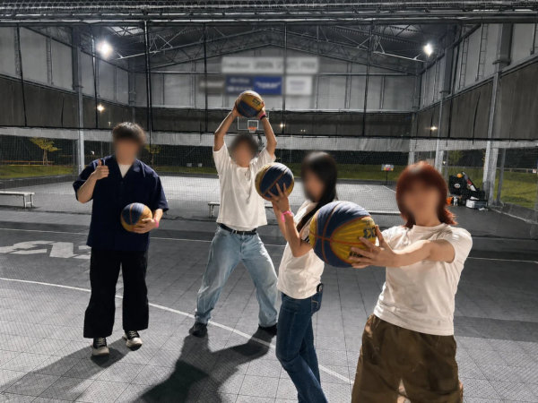 屋外のバスケットボールコートで、4人の若者がそれぞれバスケットボールを持ってポーズをとっている