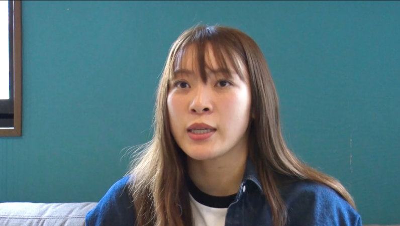 ティールブルーの壁を背景に、デニムシャツを着た若いアジア人女性のバストアップポートレート