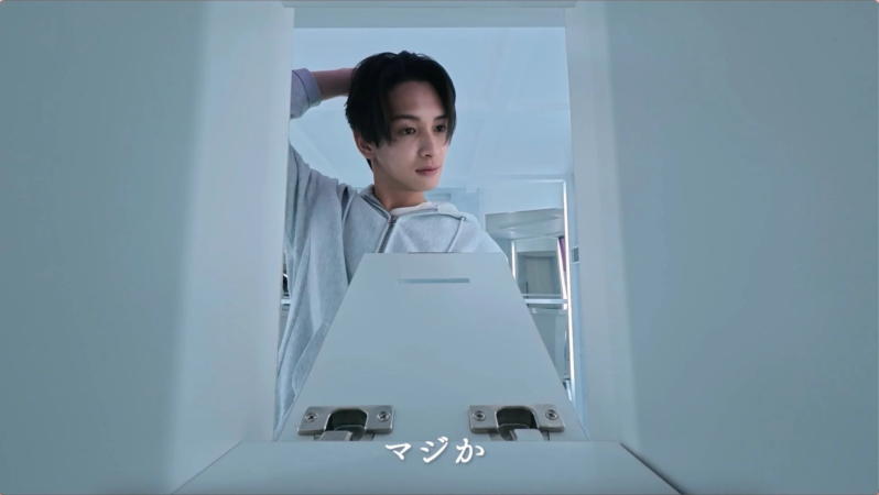 グレーのパーカーを着た若い男性が、白いキャビネットや箱の中を覗き込み、驚いたような表情
