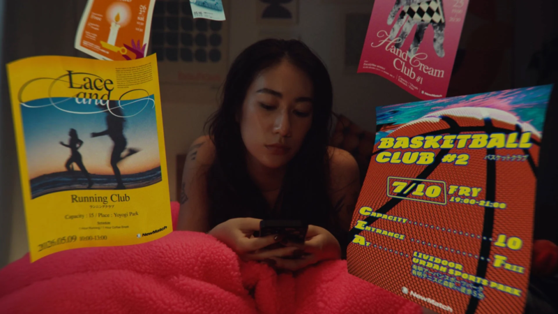 ベッドに横たわりスマートフォンを見る女性の周りに、ランニング、バスケットボール、ハンドクリームなどのイベントポスターが浮遊している。